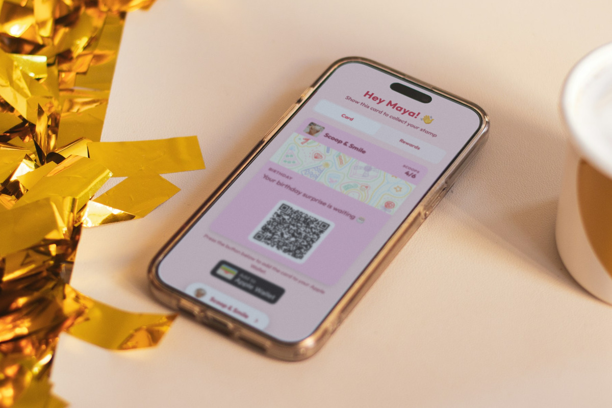 Illustration: a phone on a cream table beside gold confetti and a white cup, showing a Scoop & Smile loyalty card on the customer's birthday with the line 'Your birthday surprise is waiting'