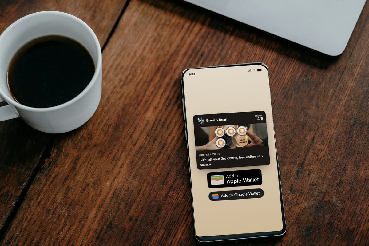 Illustration: a phone lying on a wooden café table next to a cup of black coffee, showing the Brew & Bean loyalty card at 4 of 6 brews with the line "50% off your 3rd coffee, free coffee at 6 stamps" and Add to Apple Wallet and Add to Google Wallet buttons