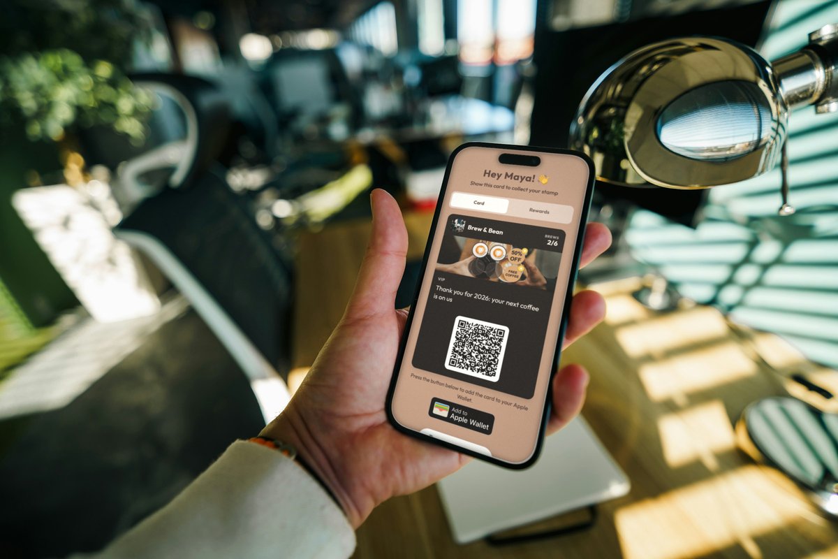 Illustration: a hand holding a phone in a sunny café, showing a Brew & Bean loyalty card with the message Thank you for 2026: your next coffee is on us