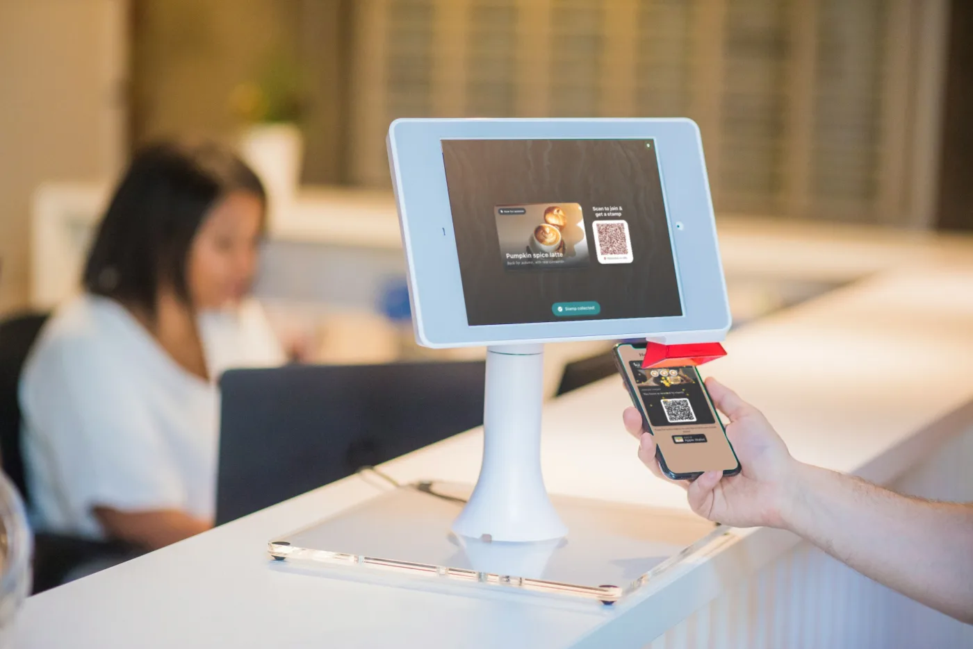Illustration: a customer holds a phone showing a loyalty card with confetti next to an iPad kiosk that says Stamp collected