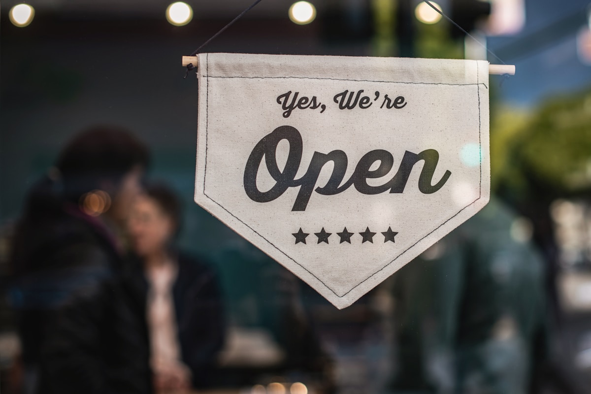 Yes We're Open fabric pennant sign hanging in a small business shop window with warm bokeh lights