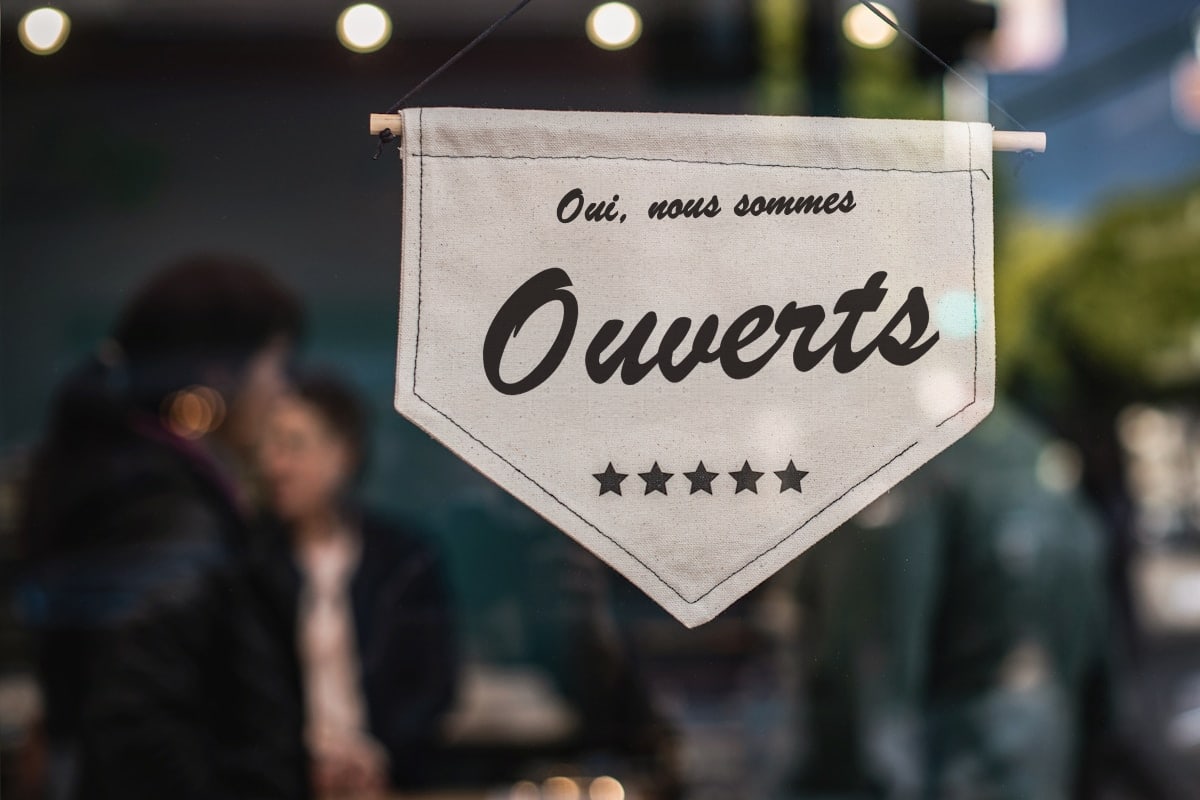 Panneau « Oui, nous sommes ouverts » accroché dans la vitrine d'un commerce de proximité avec un éclairage chaleureux en arrière-plan