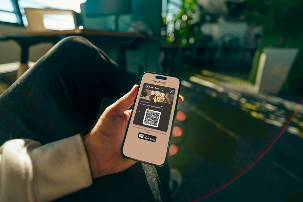 A hand holding an iPhone that shows a Brew & Bean loyalty card with 3 of 6 stamps, a reward to claim and an Add to Apple Wallet button