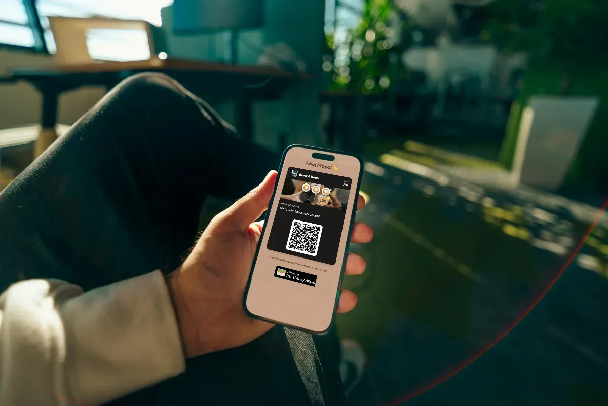 Ilustrace: ruka drží telefon s věrnostní kartou kavárny, hvězdičkovými konfetami a tlačítkem pro přidání do Apple Wallet.