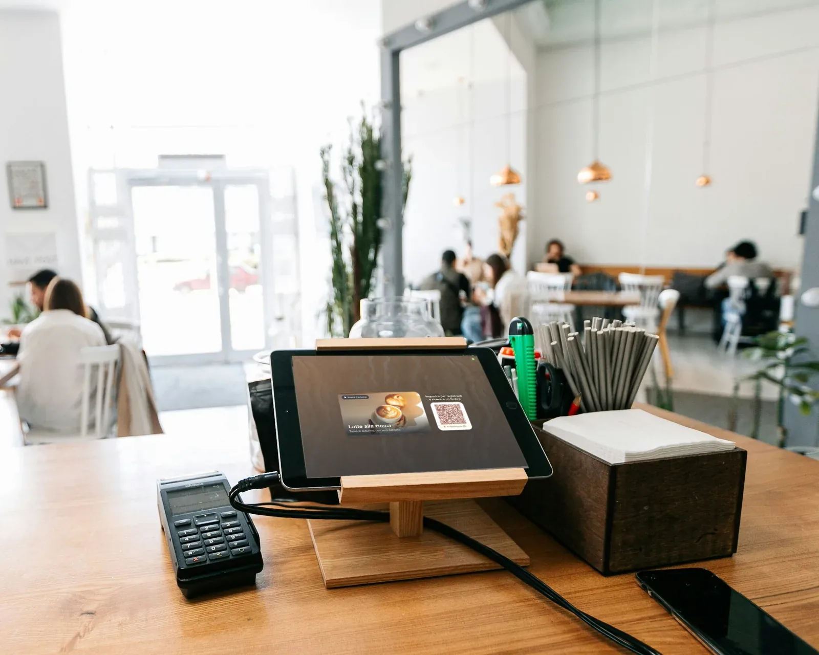 Illustrazione: un iPad su un supporto di legno al bancone di un bar, con una promo pumpkin spice latte e un QR code per iscriversi e ricevere un timbro.