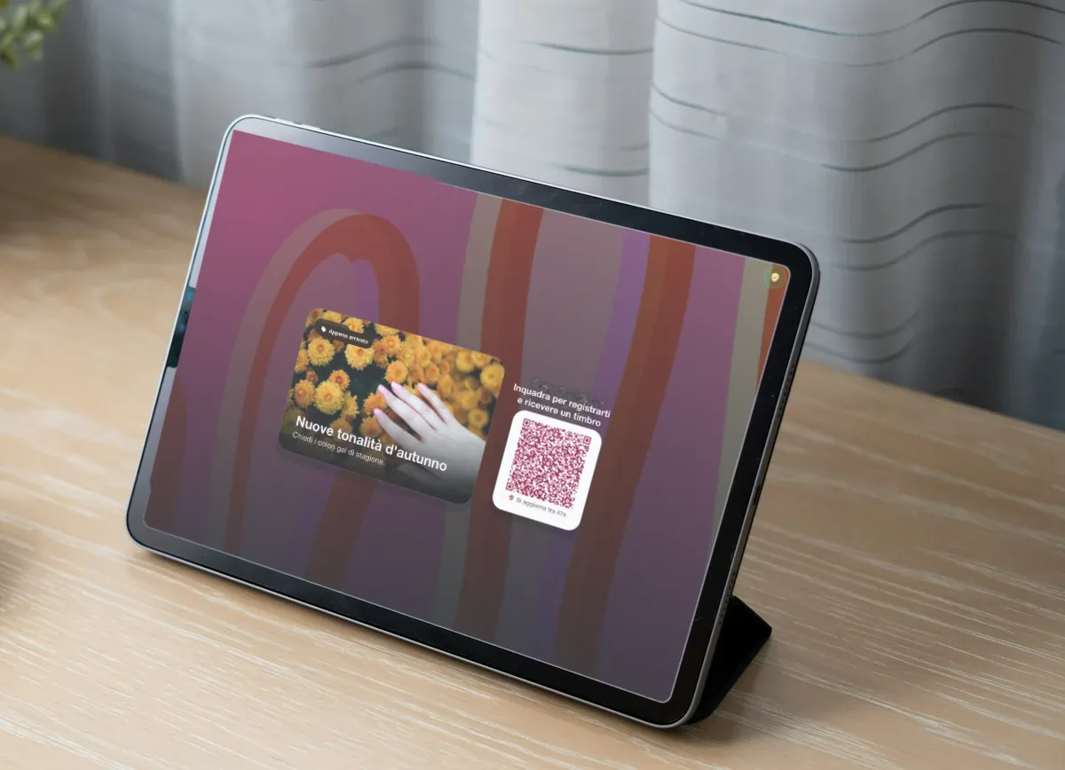 Illustrazione: un iPad su una scrivania di legno chiaro con la promo di un centro unghie, "New autumn shades", e un QR code per iscriversi e ricevere un timbro.