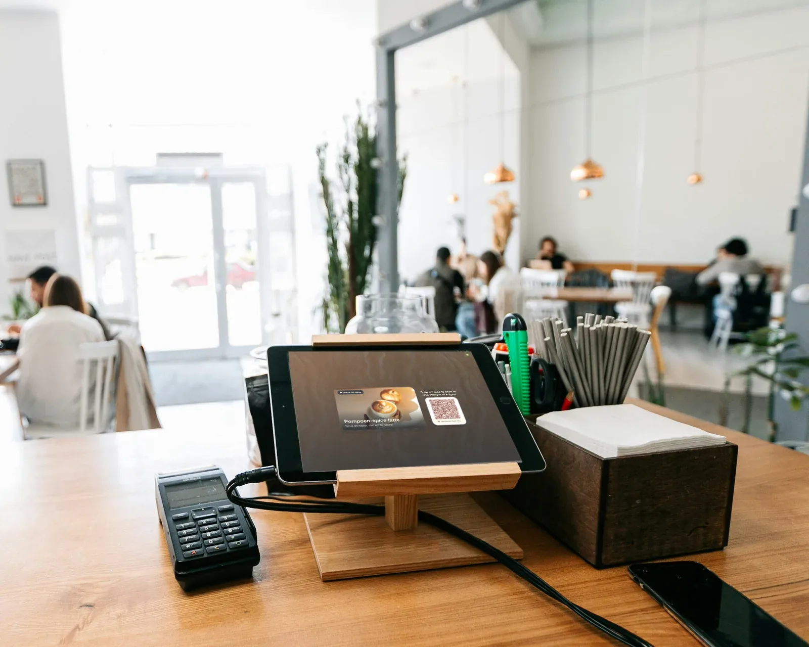 Illustratie: een iPad op een houten standaard aan de toonbank van een koffiezaak, met een pumpkin spice latte-actie en een QR-code om mee te doen en een stempel te halen.