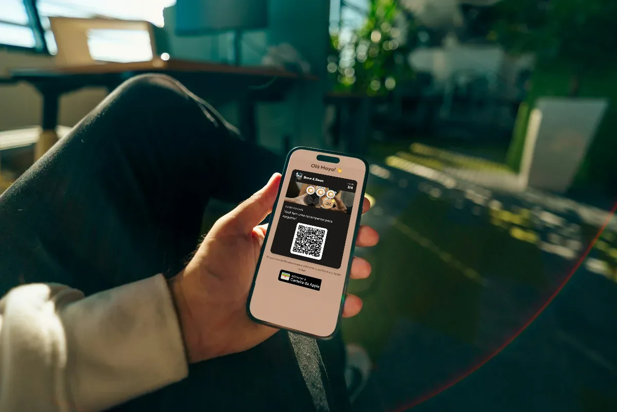 Ilustração: uma mão segura um celular com o cartão de fidelidade de uma cafeteria, confete de estrelas e um botão para adicionar à Apple Wallet.